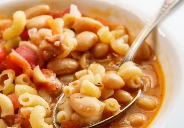 Un cucchiaio raccoglie un saporito piatto di pasta e fagioli, con maccheroni, fagioli bianchi e pomodoro in un brodo ricco.