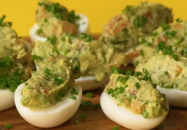 Jajka faszerowane guacamole, udekorowane szczypiorkiem, wyglądają apetycznie na drewnianej desce.
