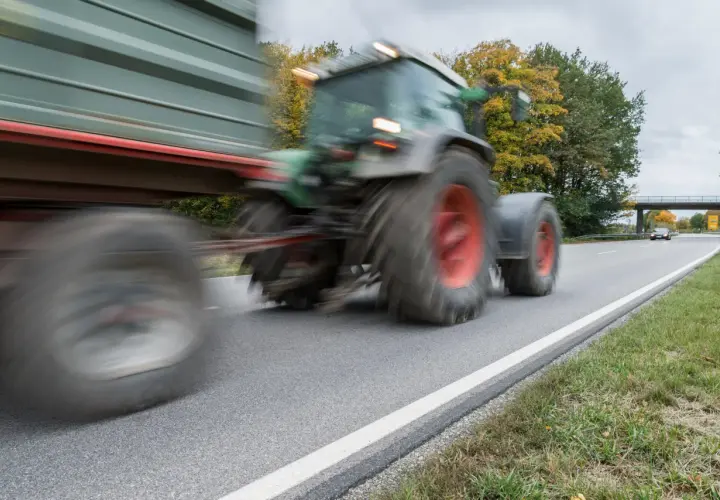 Ein Traktor mit Anhänger fährt auf einer Landstraße. Ab wann darf man Traktor fahren? Das ist eine wichtige Frage für junge Landwirte.