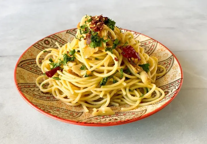 Un plato de spaghetti aglio e olio, con ajo laminado, perejil fresco y hojuelas de chile rojo, servido en un plato decorado.