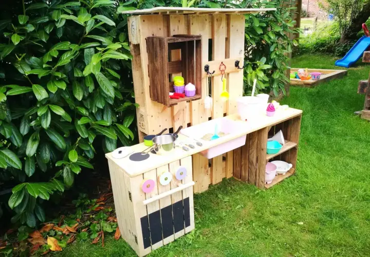 Kreative alte Weinkisten Deko Ideen: Kinderküche aus Paletten und Kisten im Garten, mit Spielzeuggeschirr und Sandkasten im Hintergrund.