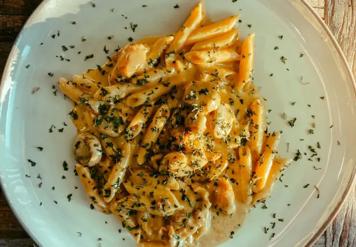 Penne w kremowym sosie z kurczakiem i pieczarkami, posypane natką pietruszki. Pyszny makaron, z którego jest zrobiony, zachwyca smakiem.