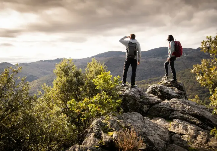Deux randonneurs contemplent un paysage montagneux depuis un promontoire rocheux, profitant d'une vue panoramique.