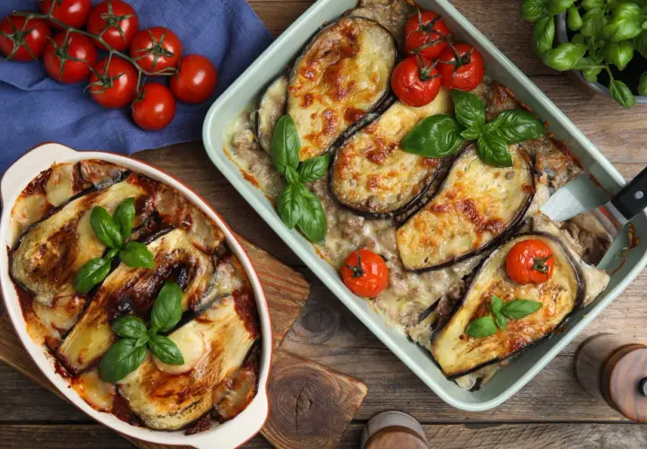 Deux plats d'aubergine à la parmesane au four, dorés et gratinés, garnis de tomates cerises et de basilic frais.