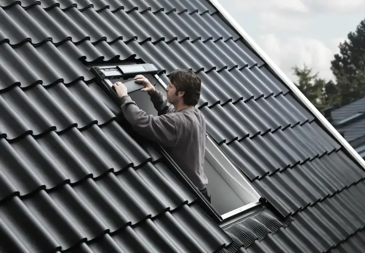 Uomo sul tetto che installa una finestra, la casa prende luce dal tetto.