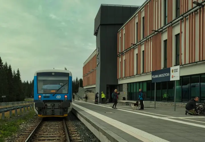 Niebieski pociąg na peronie Polany Jakuszyckiej, najwyżej położonej stacji kolejowej w Polsce. W tle nowoczesny budynek i las.