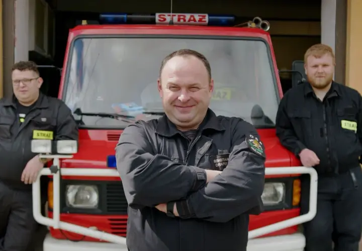 Trzech strażaków OSP pozuje przed wozem strażackim.