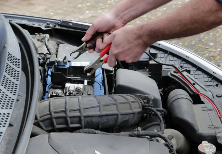 Ręce podłączają kable rozruchowe do akumulatora, bo diesel nie odpala za pierwszym razem.