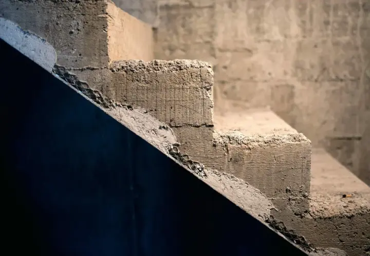 Surowe, betonowe schody wewnętrzne czekają na wyrównanie. Widać nierówności i siatkę zbrojeniową.