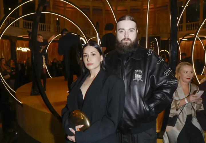 Bedoes z partnerką, która wygląda jakby była w ciąży, na złotej scenie z okręgami świetlnymi.