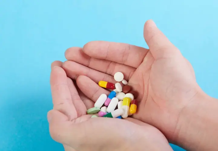 Dłonie trzymają garść kolorowych tabletek i kapsułek, wśród nich leki psychotropowe.