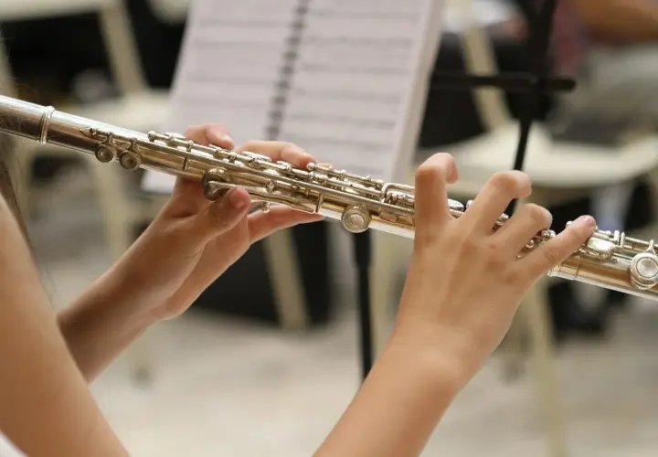 Dłonie grają na instrumencie podobnym do fletu, z nutami w tle.