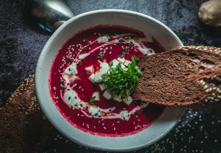 Un bol de soupe de betterave rouge polonaise, garni de crème, de dés de fromage et d'herbes, avec du pain de seigle.