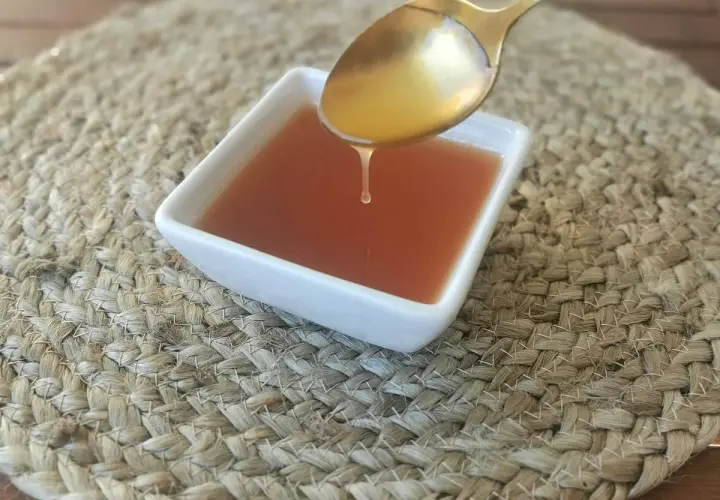 Una gota de salsa agridulce cae de una cuchara dorada a un cuenco blanco sobre una estera tejida.