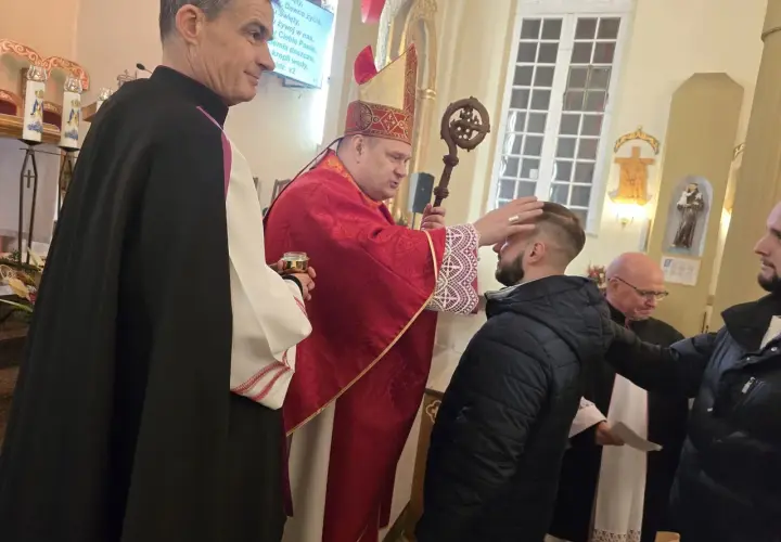 Biskup w czerwonej szacie udziela sakramentu bierzmowania młodemu mężczyźnie w kościele.
