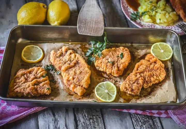 Vier goldbraune Schnitzel im Backofen, garniert mit Petersilie und Zitronenscheiben. Ein Genuss für Augen und Gaumen!
