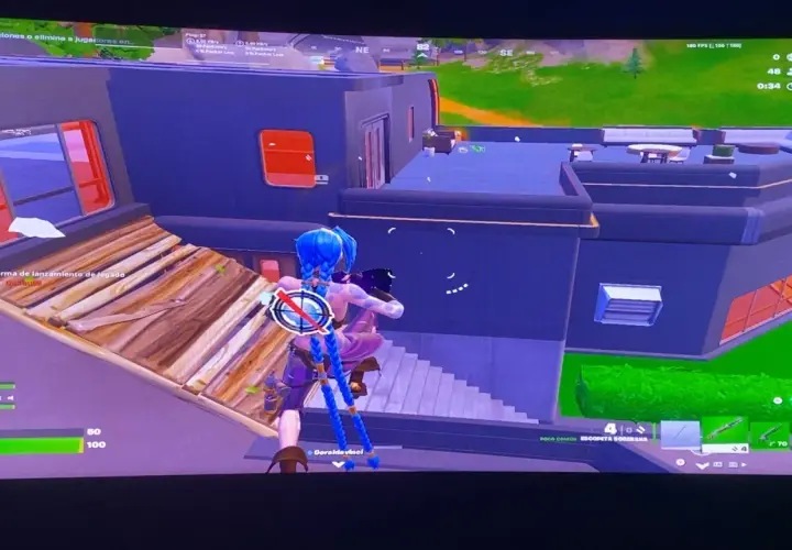 Postać z niebieskimi warkoczami w grze Fortnite buduje drewnianą rampę, celując w budynek. Opis gry Fortnite.