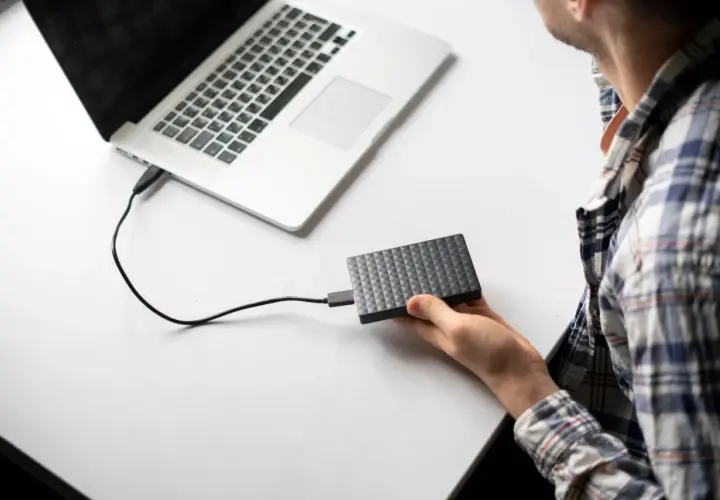 Chłopak podłącza dysk zewnętrzny do laptopa. Prosty sposób, jak podłączyć dysk zewnętrzny do laptopa, by przenieść dane.