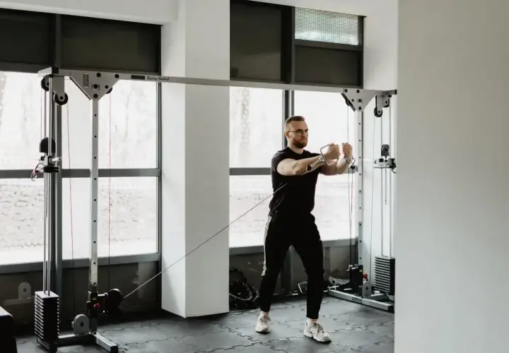 Mężczyzna w okularach wykonuje trening siłowy na wyciągu. Skupiony na ćwiczeniu, buduje siłę i wytrzymałość.