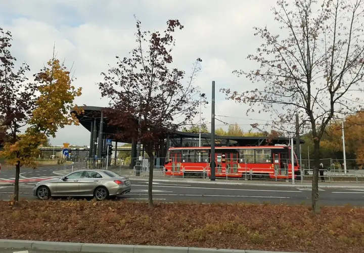 Srebrny samochód i czerwony tramwaj na przystanku, otoczone jesiennymi drzewami. Non stop big single.