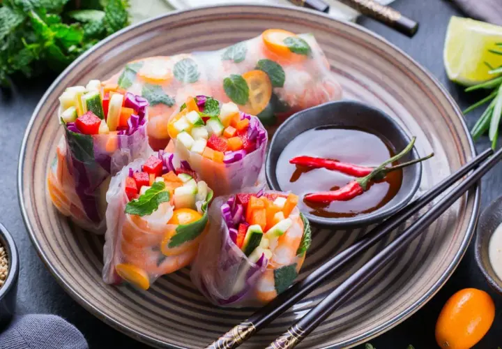 Kolorowe spring rolls z krewetkami, warzywami i miętą, podane z sosem chili i limonką. Pyszna przekąska.