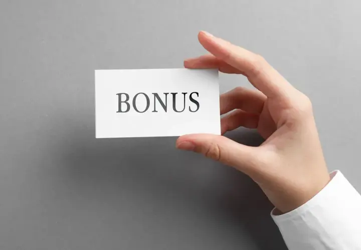 Dłoń trzyma kartkę z napisem "BONUS". To może być dodatek stażowy, który czeka na Ciebie!
