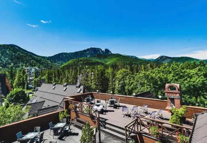 Klimatyczny hotel w górach z tarasem widokowym. Widać drewniane meble, góry i las.