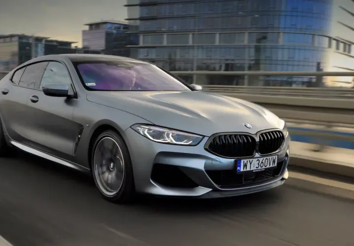 Srebrne BMW M850i sunie po moście, odbijając światła miasta w swoich lśniących szybach.