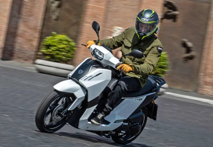 Hombre en scooter Peugeot Tweet 125, con casco y chaqueta verde, circulando por una calle.