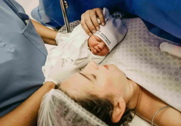 Mommy and baby bonding after cesareo. A nurse's hand gently holds the newborn's hat.
