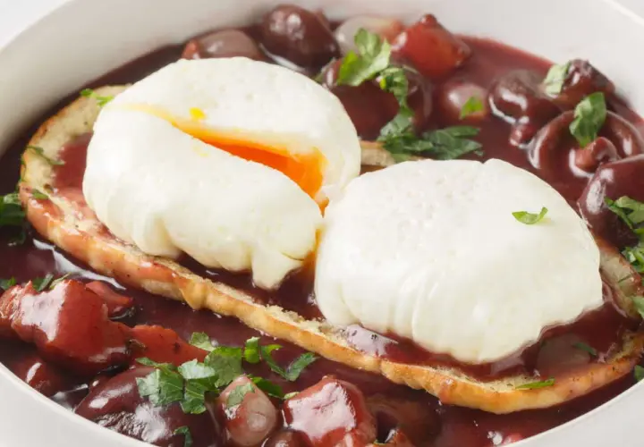 Un œuf meurette, deux œufs pochés sur toast, baignant dans une sauce au vin rouge avec lardons et oignons.