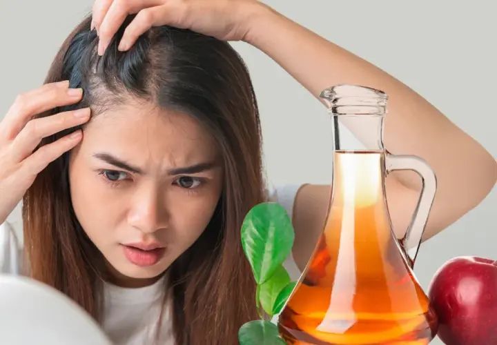 Mujer preocupada revisa su cabello. A su lado, una botella de vinagre de manzana para el pelo y una manzana roja.
