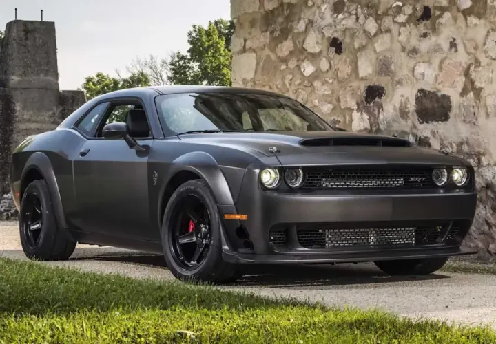 Mroczny Dodge Challenger Demon, z potężną maską i agresywnym grillem, stoi przed kamienną ścianą.