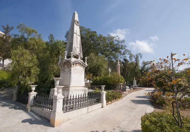 Un obelisco y monumentos se alzan en el cementerio de los ingleses, un lugar sereno bajo un cielo azul.
