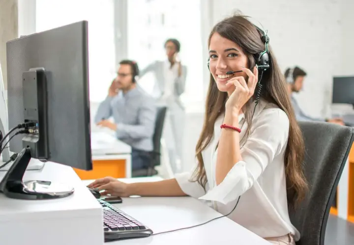 Eine freundliche Callcenter-Mitarbeiterin lächelt in die Kamera. Sie sitzt am Schreibtisch und spricht ins Headset. Sie hilft Kunden, die vielleicht auch mal Werbung widersprechen möchten.