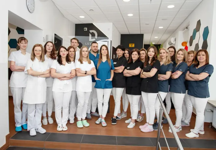 Grupa uśmiechniętych dentystów w białych i granatowych uniformach stoi w gabinecie.