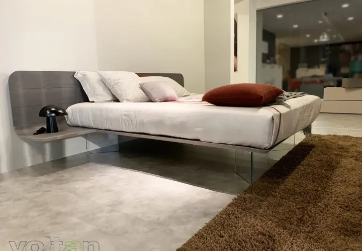 Un letto sospeso come funziona: design moderno con testiera in legno, comodino integrato e gambe in vetro trasparente.