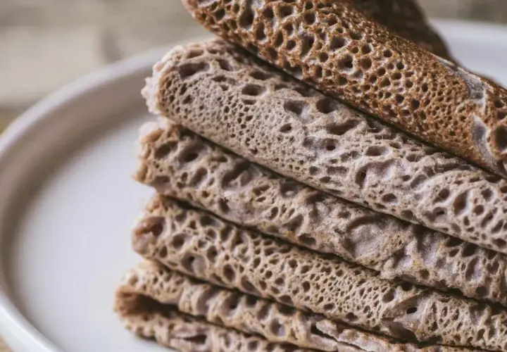 Pile de crêpes et de galettes, certaines roulées, d'autres pliées, avec une texture alvéolée. Un délice qui rappelle le goût de l'andouille.
