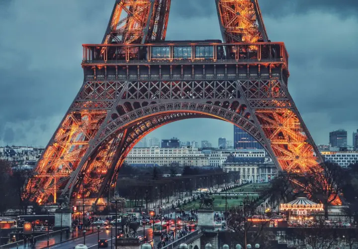Eiffel rozświetlona pomarańczowym blaskiem, z widokiem na paryskie ulice i budynki.