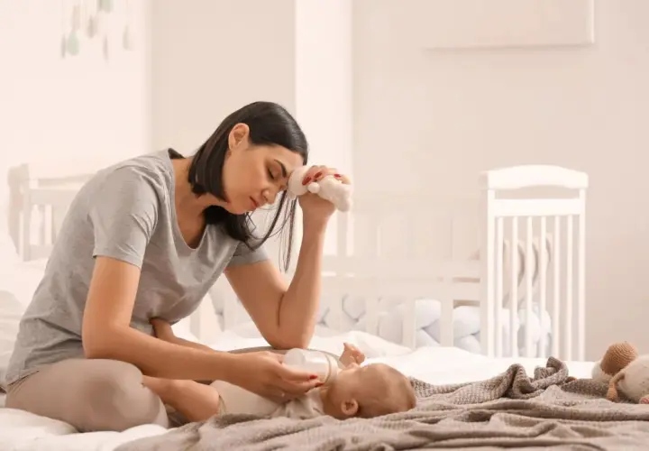 Madre esausta che allatta il neonato, con un peluche in mano, simbolo della sua lotta contro la depressione post partum.