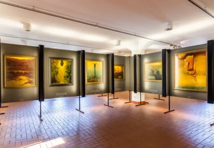 Wystawa obrazów Beksińskiego w galerii, z widocznymi dziełami w żółtych i brązowych barwach.