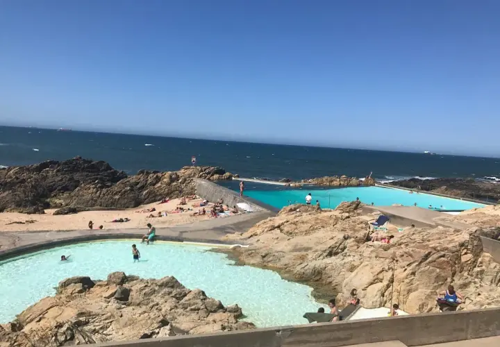 Piscinas naturais na praia de Matosinhos, Porto, com pessoas a nadar e a apanhar sol.