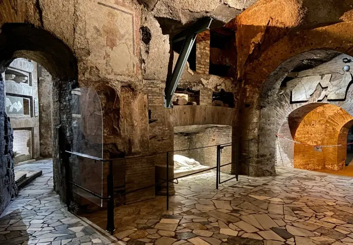 Intérieur des catacombes San Callisto. Un sarcophage blanc repose sous un arc de briques, dans un dédale de couloirs aux fresques anciennes.