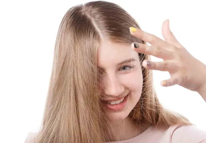 Chica sonriente con cabello rubio que se toca la frente, buscando cómo quitar la electricidad del pelo.