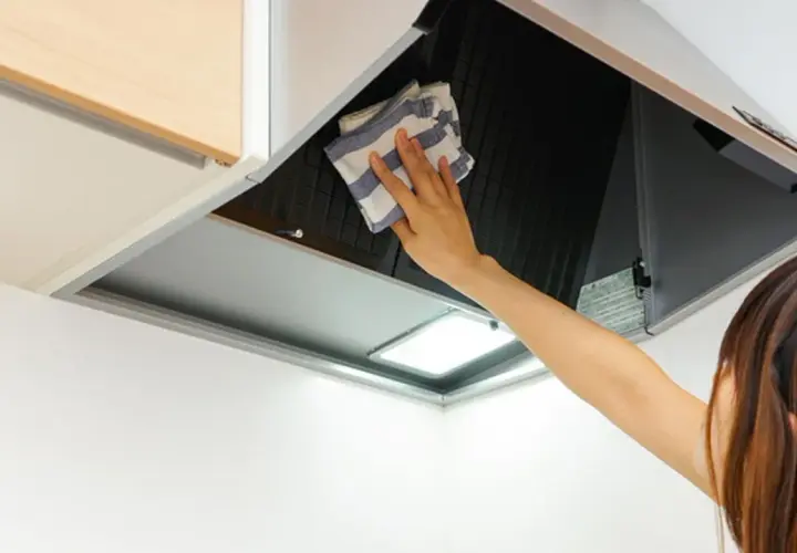 Mano limpiando campana extractora por fuera con un paño a rayas.