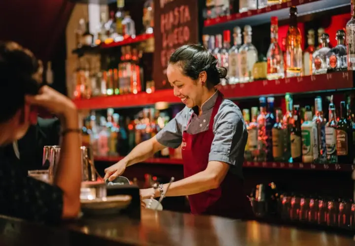 Uśmiechnięta barmanka w Gdańsku przygotowuje drinka. Zastanawiasz się, ile zarabia barman w Gdańsku?
