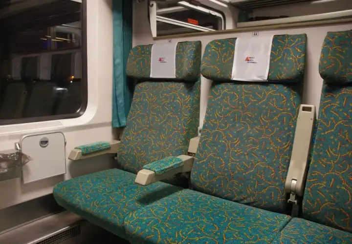 Wnętrze wagonu osobowego PKP Intercity z wygodnymi siedzeniami w turkusową tapicerkę.