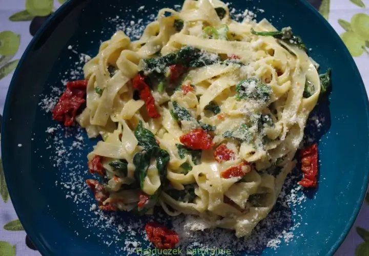 Pyszny makaron tagliatelle ze szpinakiem i suszonymi pomidorami, posypany parmezanem. Idealny na szybki obiad.