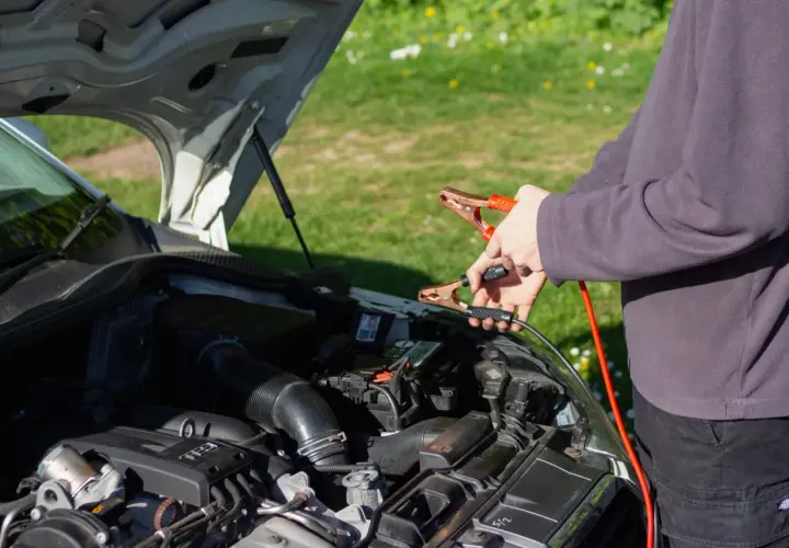 Ręce trzymające kable rozruchowe przy akumulatorze. Czy można odpalic auto na wlaczonym prostowniku?