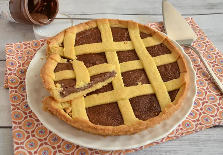 Deliziosa crostata alla Nutella con una fetta tagliata, pronta per essere gustata. Un vasetto di Nutella è visibile sullo sfondo.